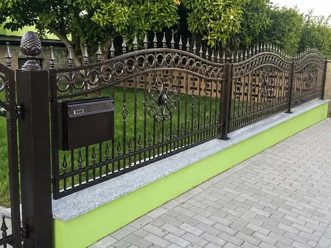 Schwarzer Schmiedezaun mit handwerklichen Ornamenten auf einem Mauersockel
